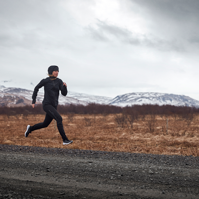 Homem a correr com roupa desportiva preta em estrada com montanhas ao fundo