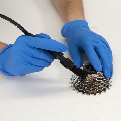 Luvas azuis a limpar cassete de bicicleta com escova preta