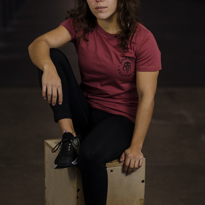 Pessoa sentada numa caixa de madeira com t-shirt vermelha e calças pretas