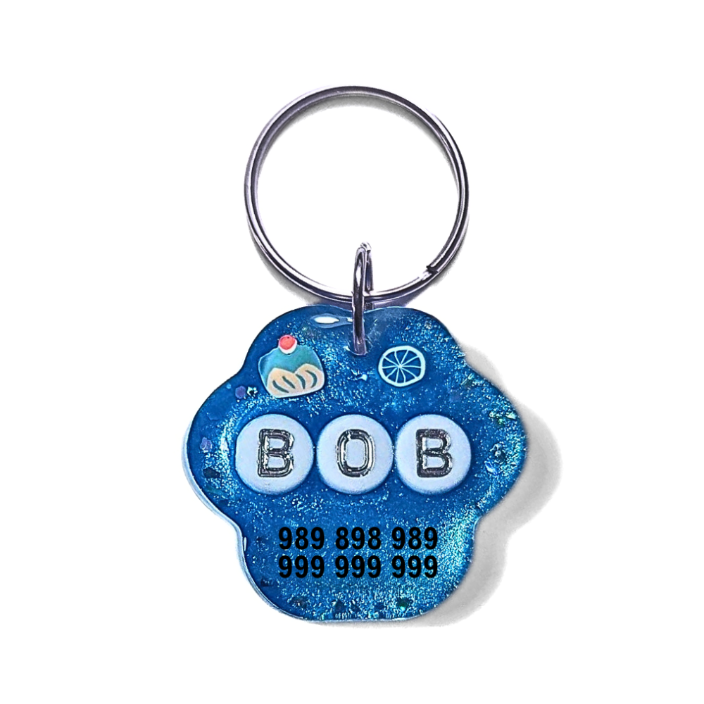 Chaveiro azul forma pata com letras 'BOB' e números de telemóvel