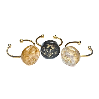 Três anéis com pedras redondas marmorizadas castanho, preto e cinza claro com detalhes dourados