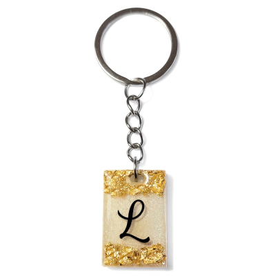Chaveiro retangular transparente com partículas douradas e letra L preta