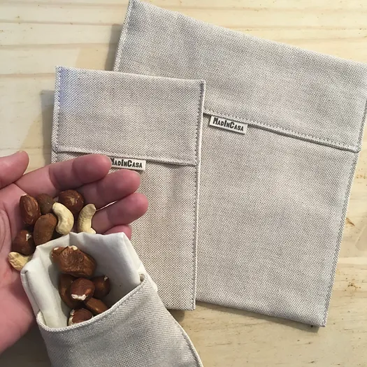 Três bolsas reutilizáveis de tecido bege com frutos secos numa mão e etiqueta MADIN CASA