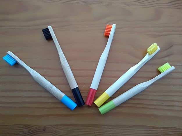 Cinco escovas de dentes de madeira com cerdas coloridas sobre superfície de madeira