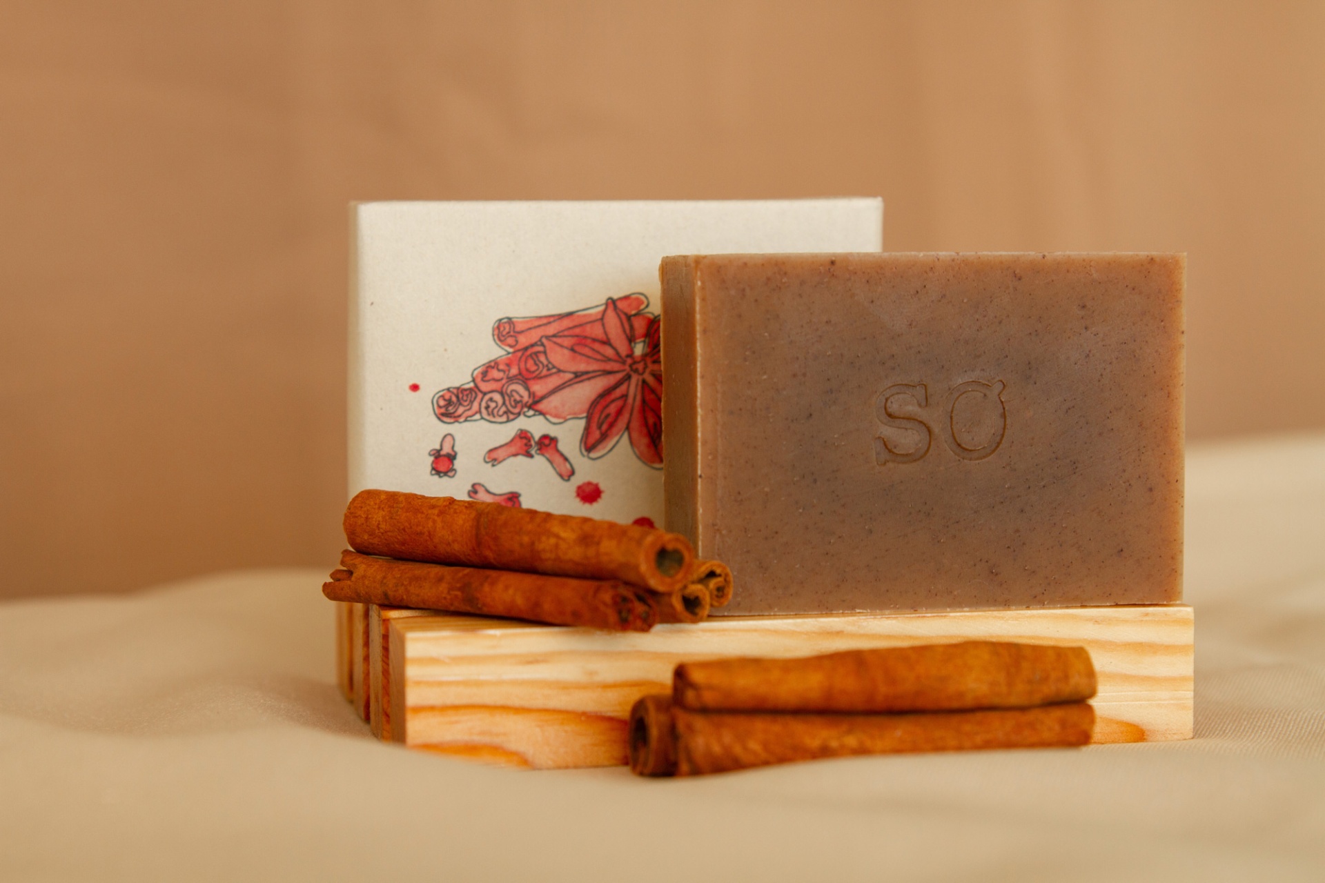 Sabonete marrom com gravação SO, paus de canela e caixa branca com ilustração
