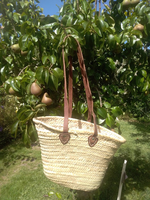 Cesto de palha com alças de couro pendurado numa árvore frutífera