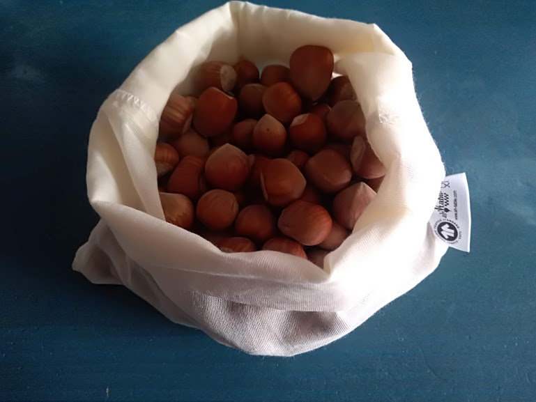 Saco branco de pano cheio de avelãs com casca marron