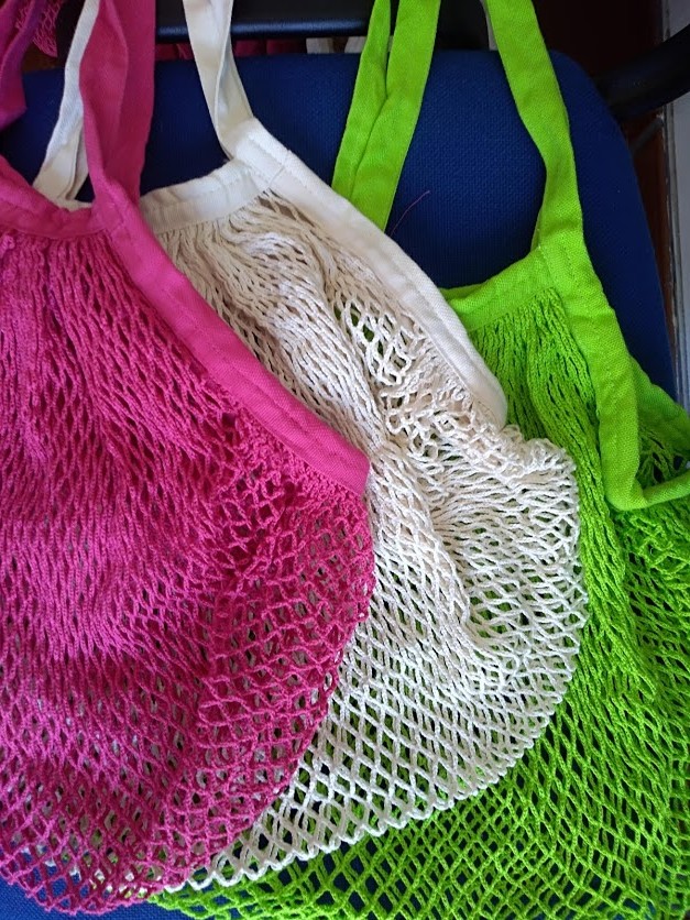 Sacos de rede coloridos em tecido rosa, branco e verde sobre fundo azul