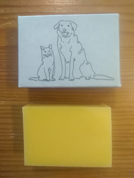 Barra de sabonete amarelo com caixa branca ilustrada com gato e cão