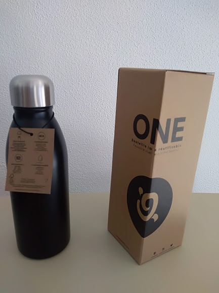 Garrafa térmica preta com tampa prateada ao lado de embalagem castanha com texto ONE e símbolo em coração preto