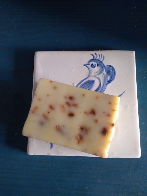 Sabonete branco com pedaços castanhos sobre azulejo branco com pássaro azul