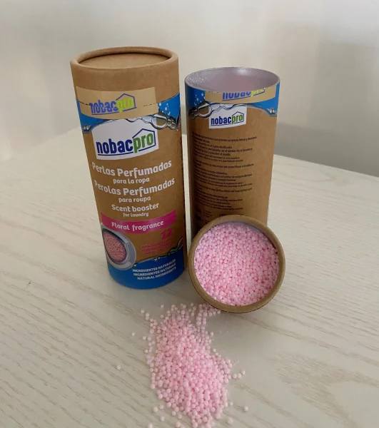 Frasco cilíndrico com pérolas perfumadas rosa spilladas numa mesa clara