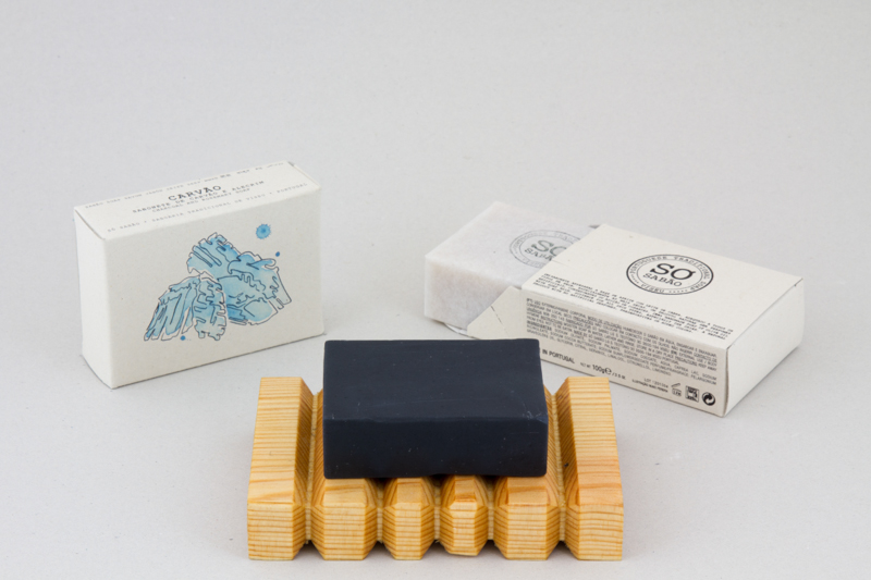 Sabonete preto e caixas brancas de embalagem em suporte de madeira.