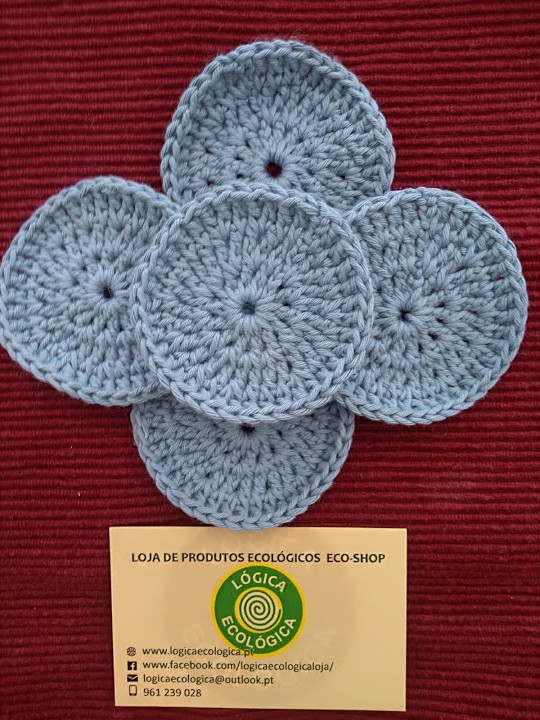 Discos de croché cinzentos em forma de flor sobre fundo vermelho com cartão da loja Lógica Ecológica