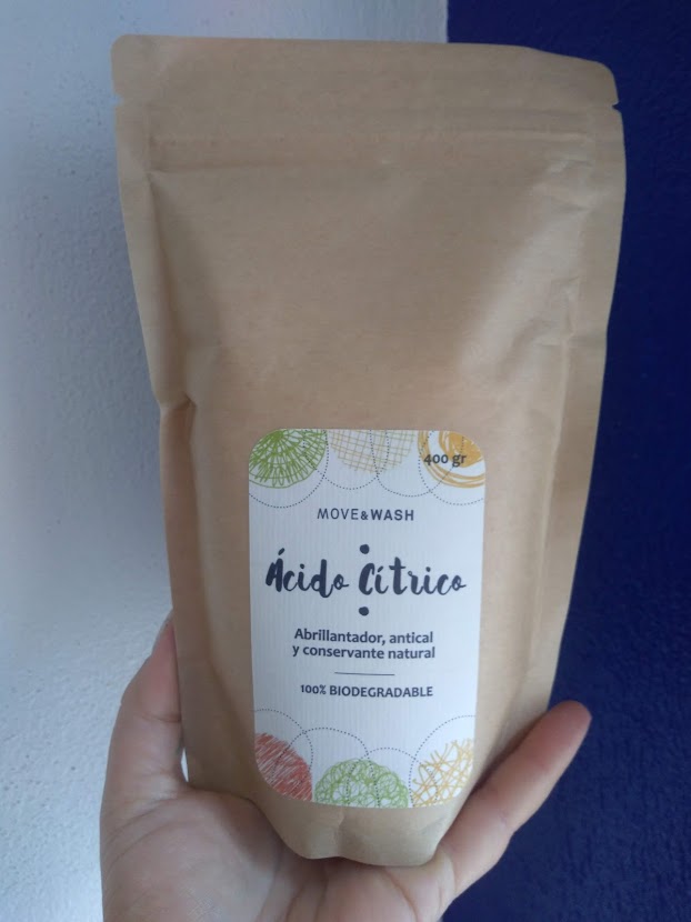 Pacote castanho de papel com etiqueta branca com texto em espanhol e português, segurado por uma mão