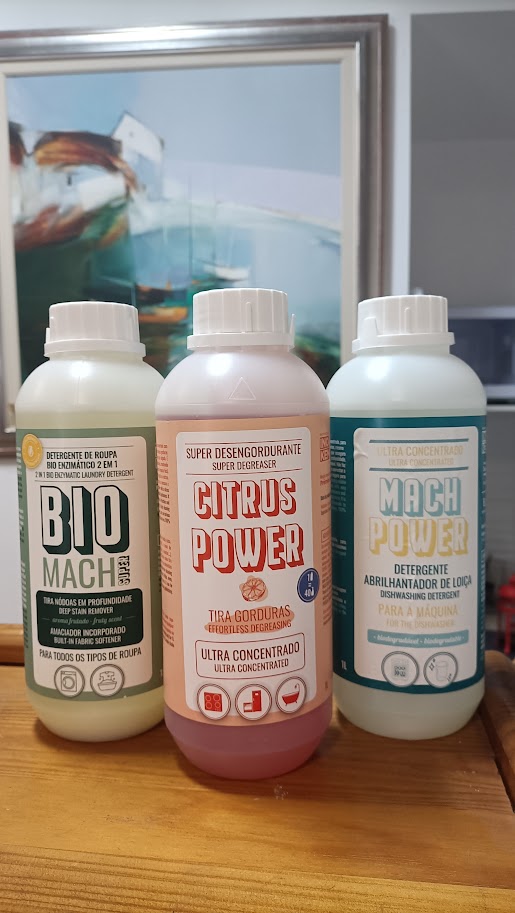 Três frascos de detergentes ultra concentrados com rótulos em português colocados sobre uma superfície de madeira à frente de um quadro emoldurado