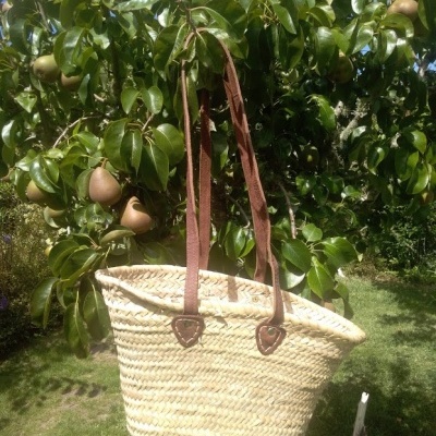 Cesto de palha com alças de couro pendurado numa árvore frutífera