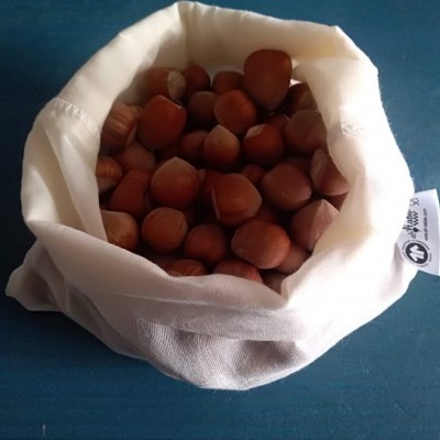 Saco branco de pano cheio de avelãs com casca marron