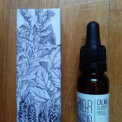 Frasco de vidro castanho com conta-gotas e caixa com ilustração botânica sobre madeira