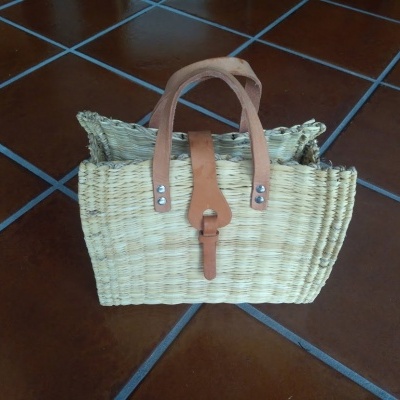 Saco de palha com alças e fecho de couro sobre chão de azulejos castanhos