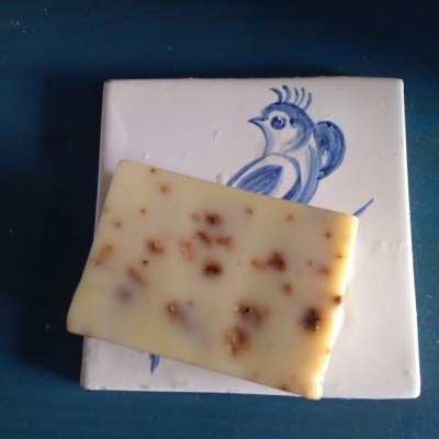 Sabonete branco com pedaços castanhos sobre azulejo branco com pássaro azul