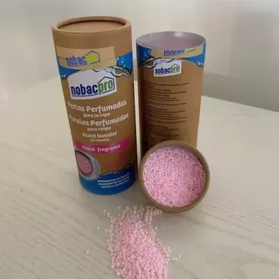 Frasco cilíndrico com pérolas perfumadas rosa spilladas numa mesa clara
