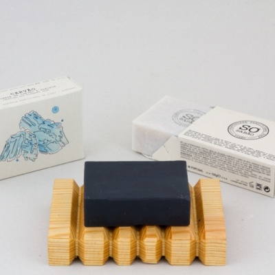 Sabonete preto e caixas brancas de embalagem em suporte de madeira.