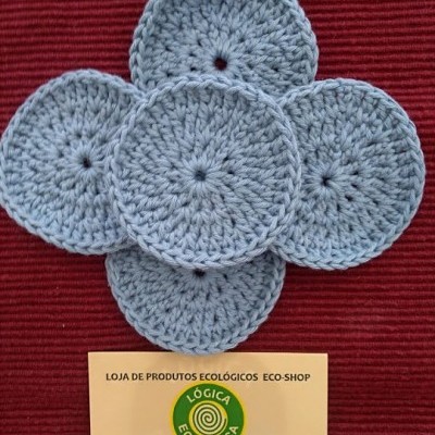 Discos de croché cinzentos em forma de flor sobre fundo vermelho com cartão da loja Lógica Ecológica