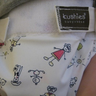 Fralda reutilizável branca para bebé com estampado de bonecos coloridos e etiqueta preta Kushies