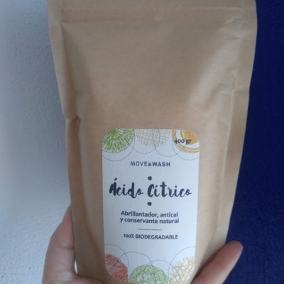 Pacote castanho de papel com etiqueta branca com texto em espanhol e português, segurado por uma mão