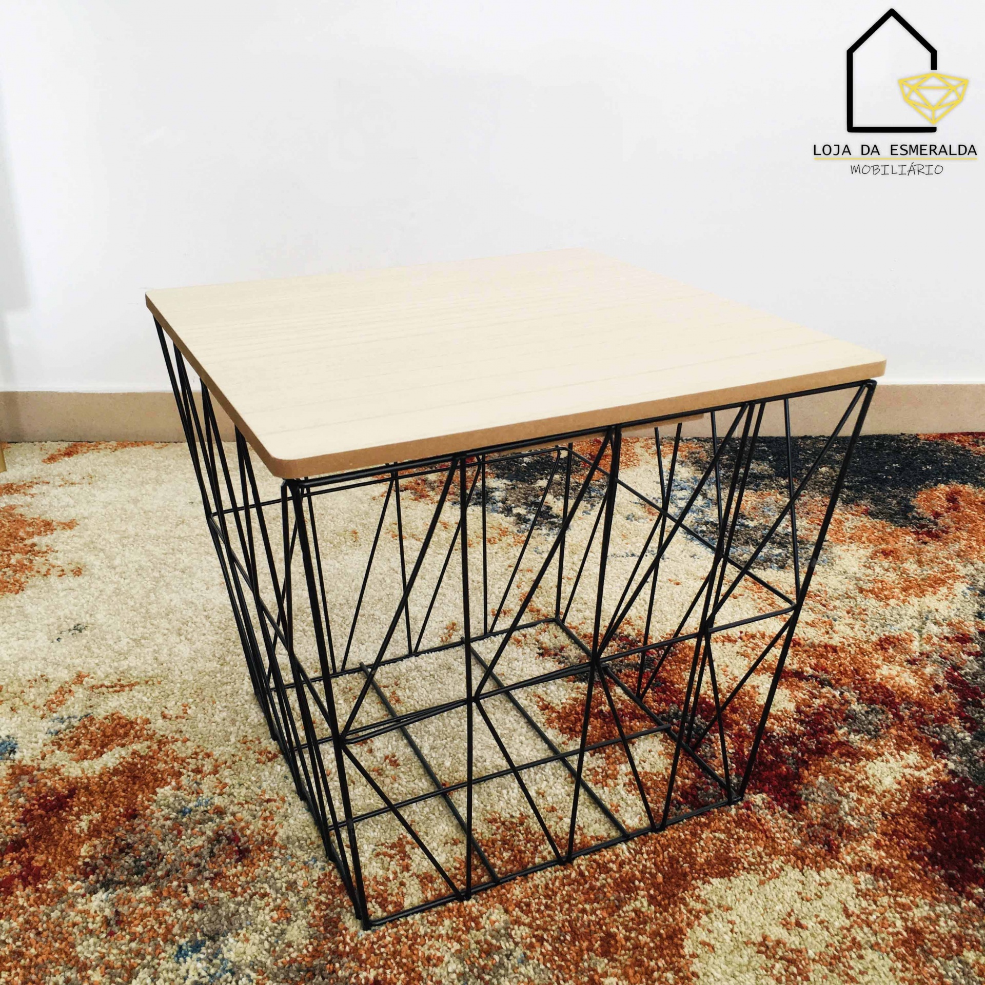 Mesa pequena com tampo de madeira clara e estrutura de arame preta sobre tapete colorido