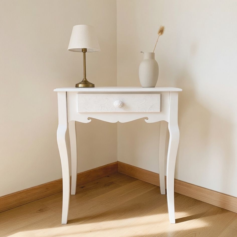 Mesa branca vintage com candeeiro e vaso numa sala clara com chão de madeira