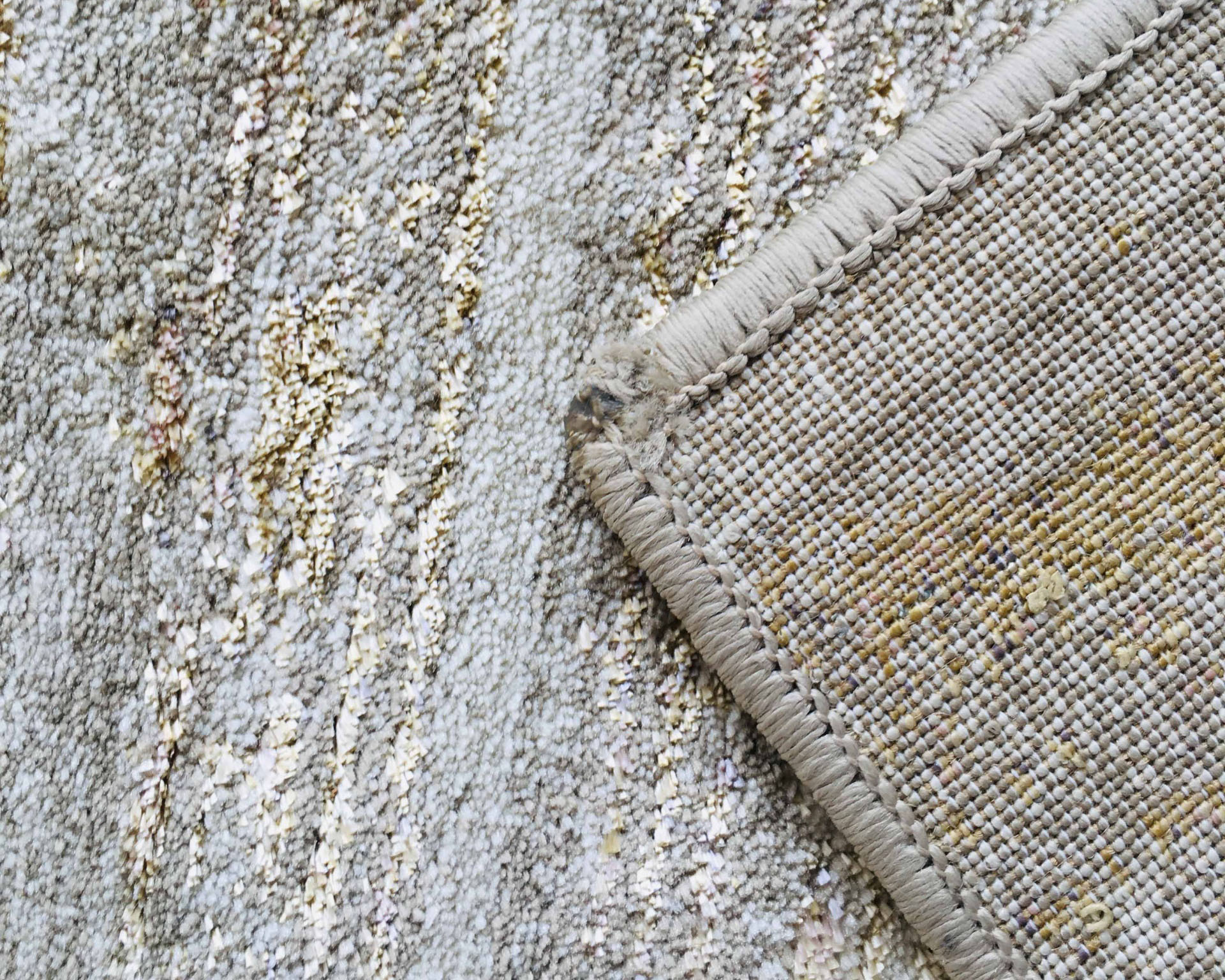 Tapete têxtil bege e cinza com borda costurada em destaque