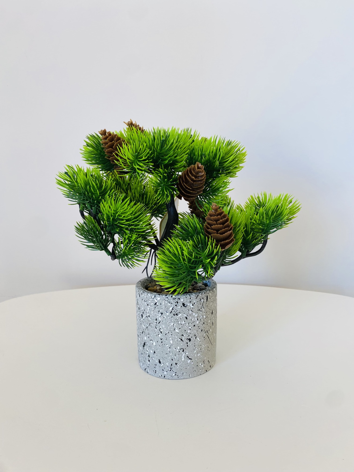 Planta artificial em vaso cinza claro com textura pontilhada sobre mesa branca