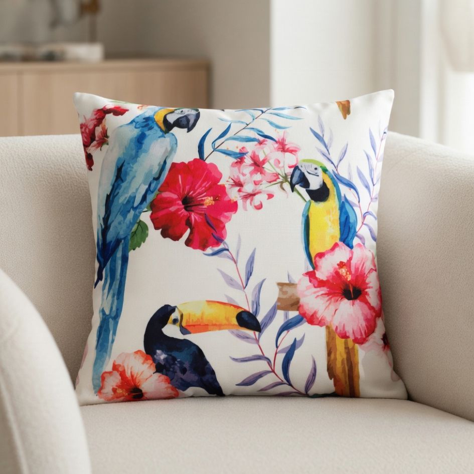 Almofada decorativa com padrão de aves tropicais e flores sobre sofá branco.