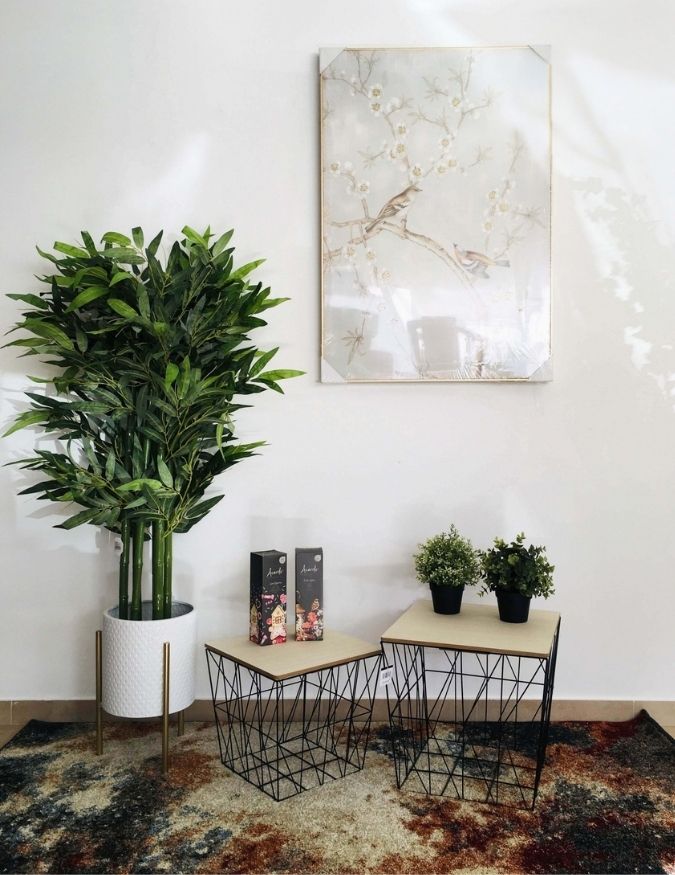 Vaso com planta artificial, mesas com tampo de madeira e estrutura metálica e quadro decorativo com pássaros