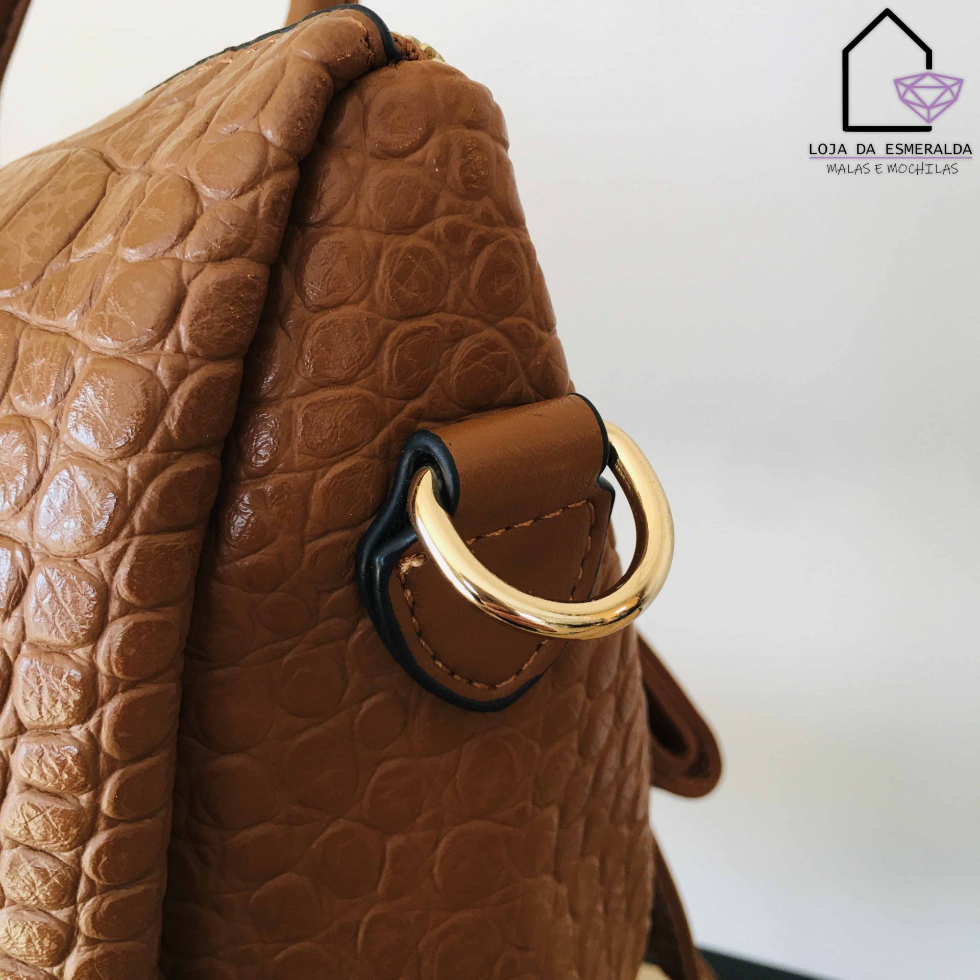 Mala castanha com textura tipo pele de crocodilo e argola metálica dourada perto do logótipo da loja