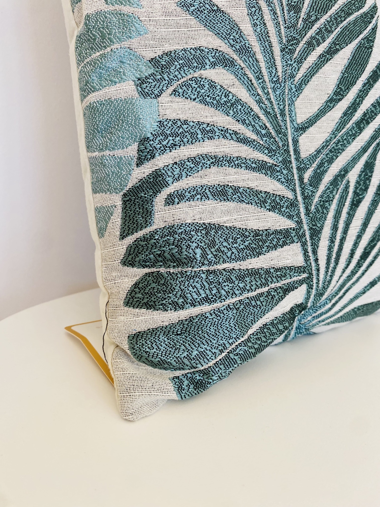 Almofada decorativa branca com padrão de folhas verdes e azuis