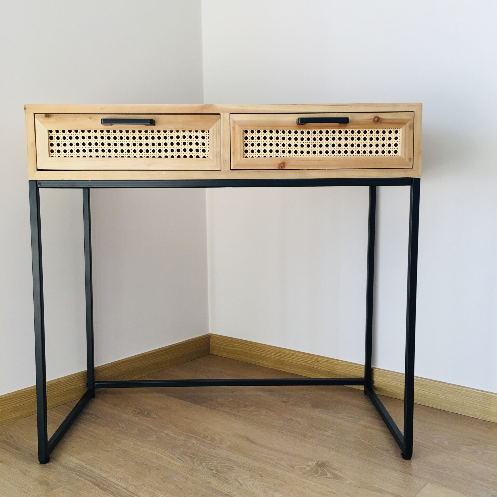 Mesa de madeira clara com duas gavetas com padrão de palhinha e pernas metálicas pretas