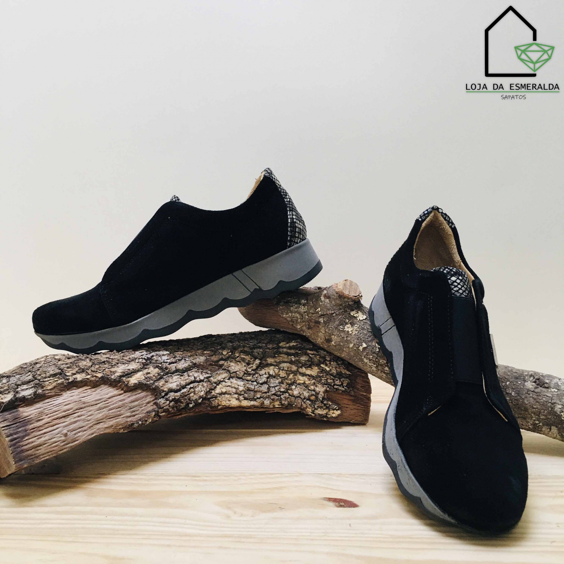 Par de sapatos pretos com sola cinzenta e detalhes em padrão cobra sobre troncos secos