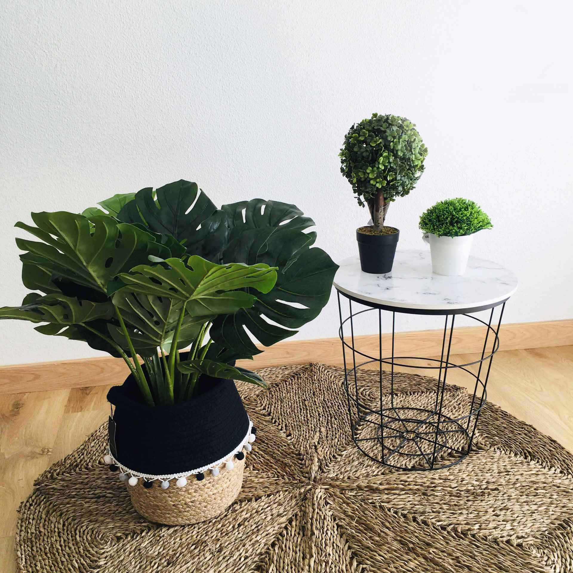 Planta artificial em vaso preto e mesa redonda com tampo branco e base de ferro preto sobre tapete de fibras naturais