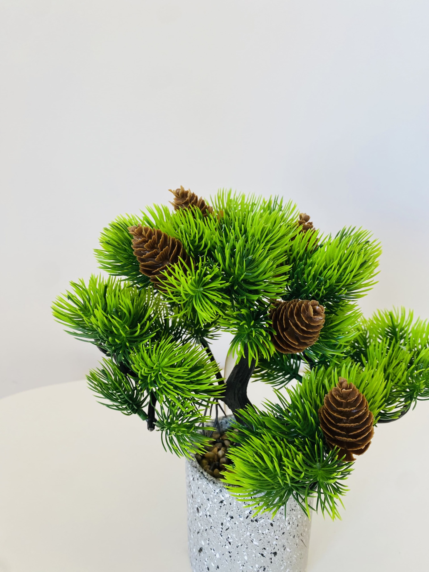 Arranjo artificial verde com cones castanhos no vaso cinzento.