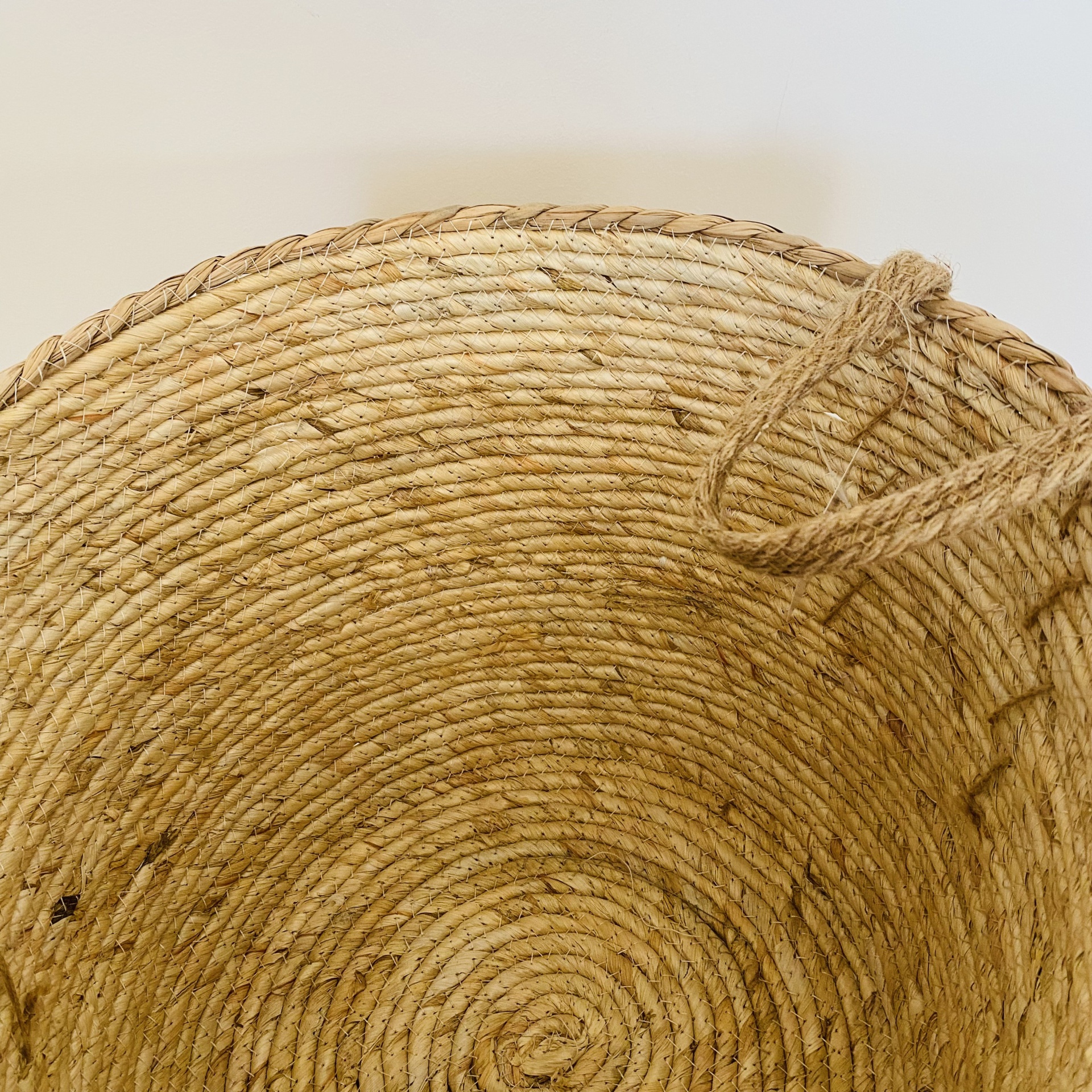 Cesto redondo de palha com alça de corda sobre fundo branco