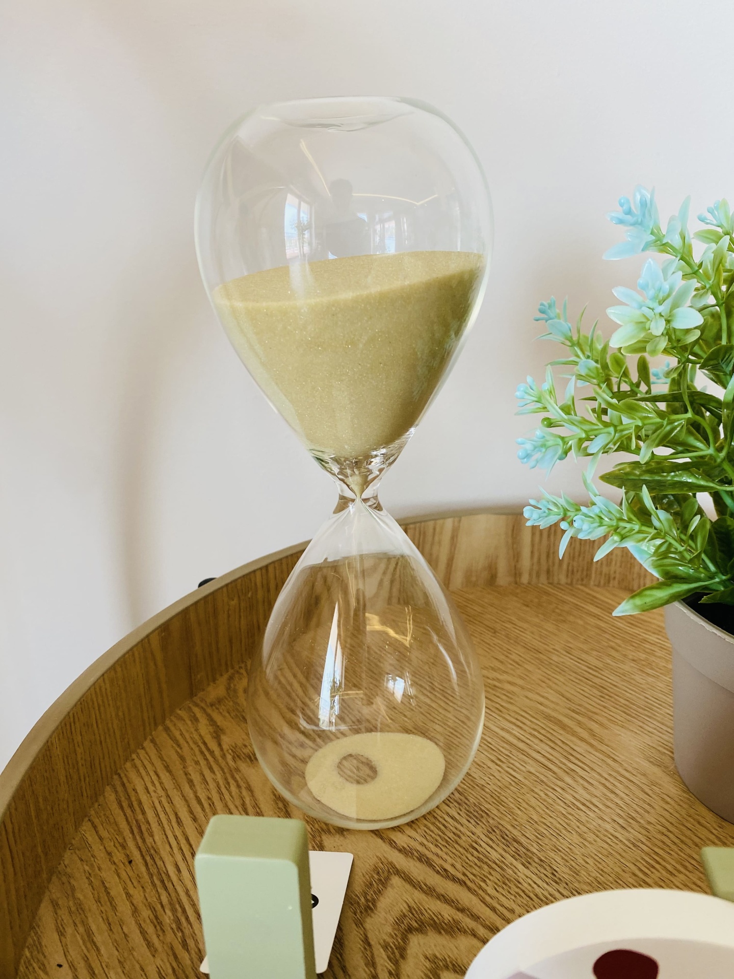 Ampulheta de vidro com areia dourada junto a planta e superfície de madeira