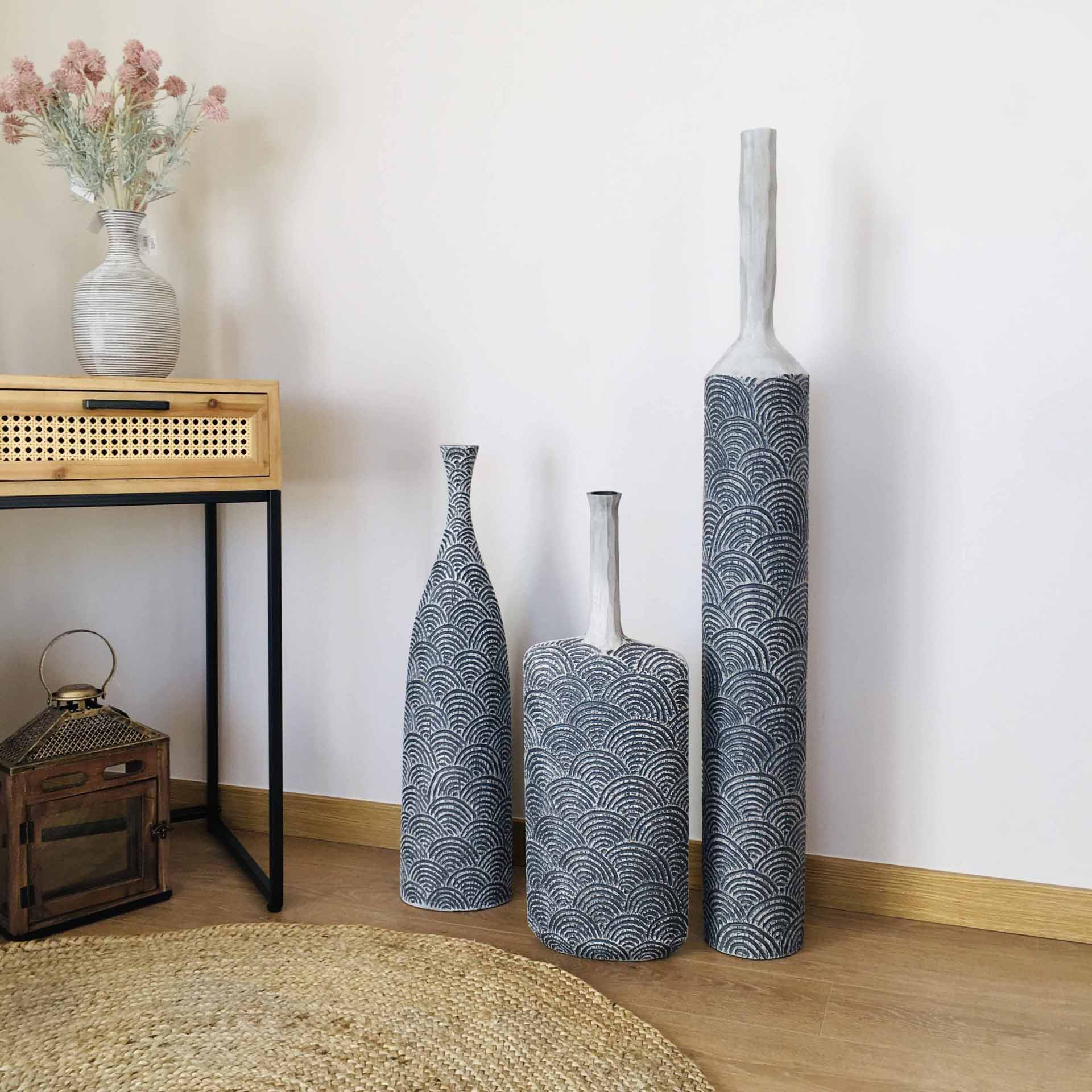 Três vasos decorativos cinza com padrão de ondas junto a móvel e tapete