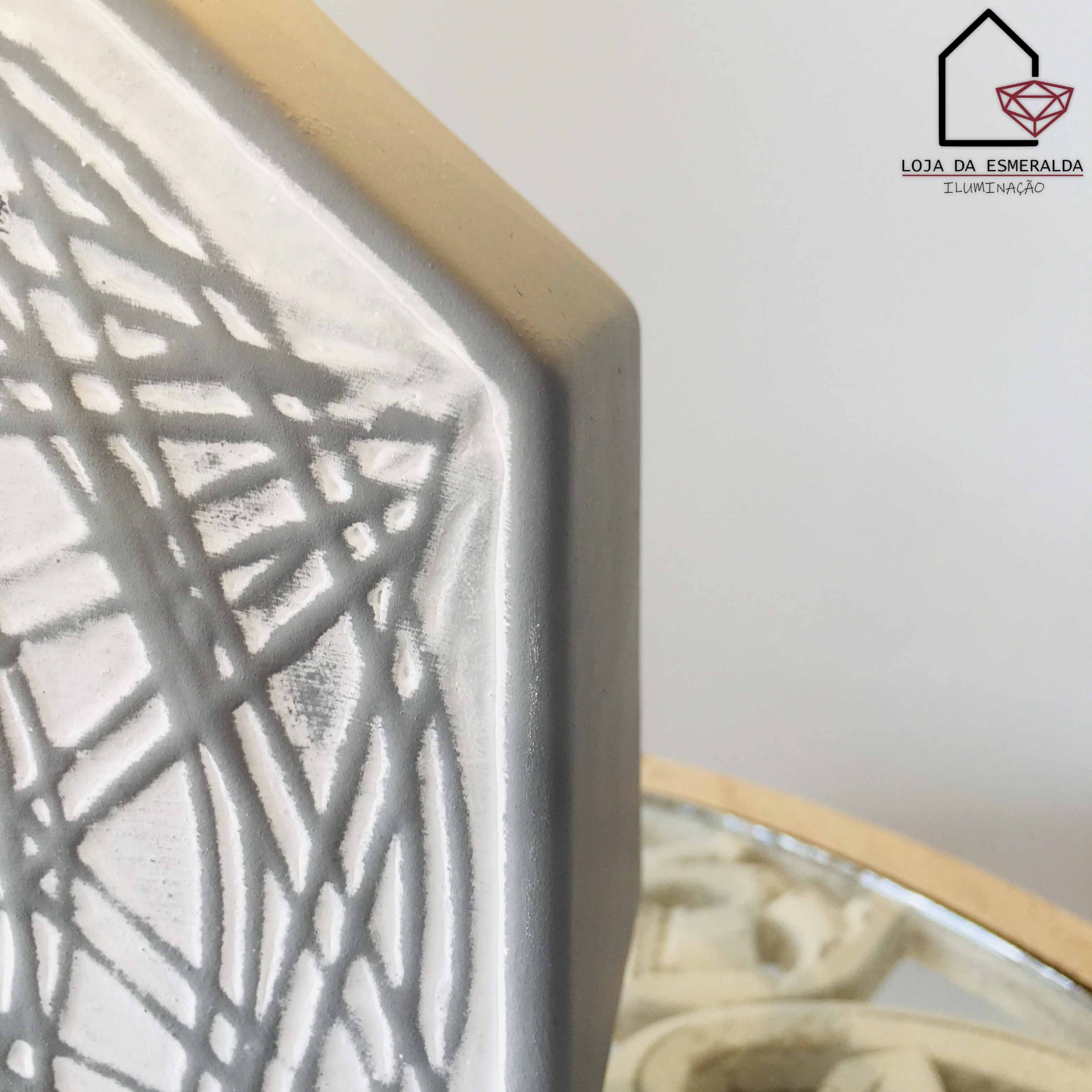 Objeto cinza texturizado com padrões lineares próximo a espelho dourado e logo de loja no fundo