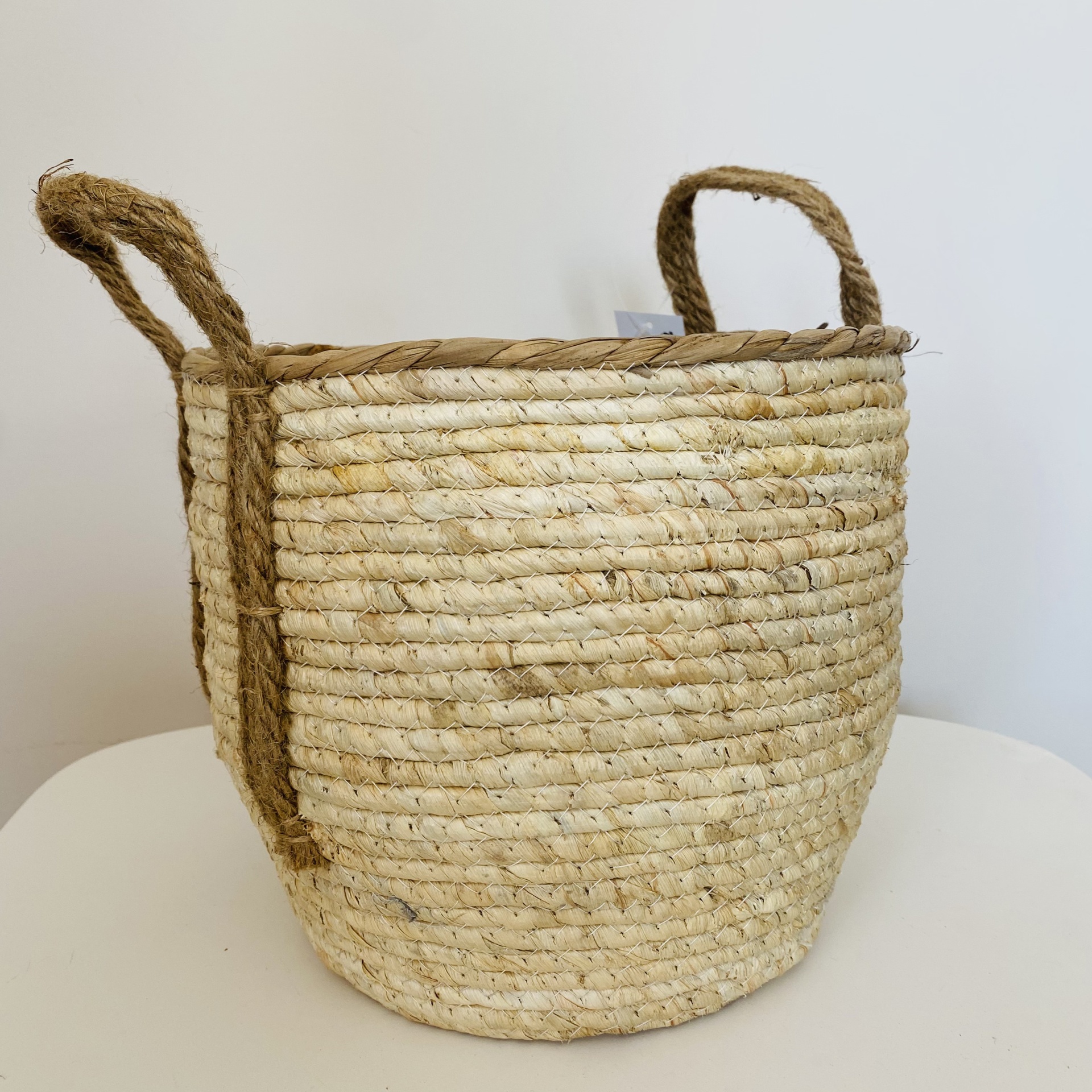 Cesto de armazenamento redondo em fibras naturais claras com pegas castanhas.