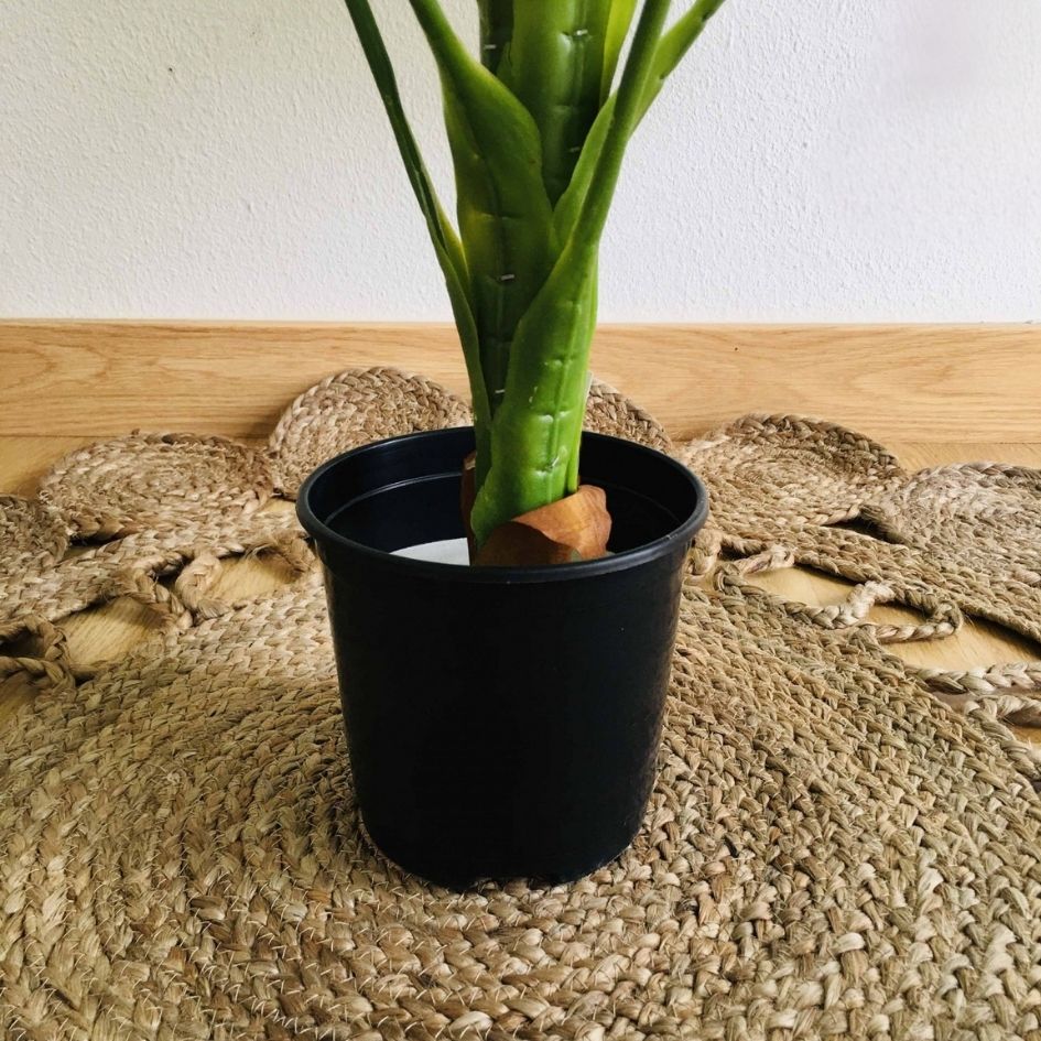 Vaso preto com planta artificial verde em tapete trançado na madeira