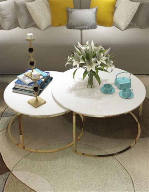 Mesas de centro redondas brancas com estrutura dourada, decoradas com flores, castiçal e conjunto de chá, em sala com sofá e almofadas.