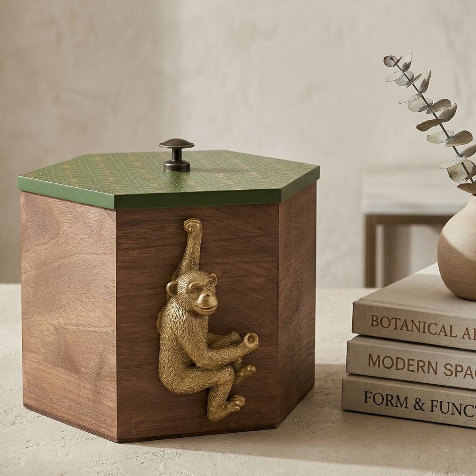 Caixa de madeira hexagonal com tampa verde e figura dourada de macaco na lateral, ao lado de livros empilhados